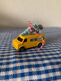 a yellow toy car with a christmas tree on the roof sitting on a blue and white checkered tablecloth