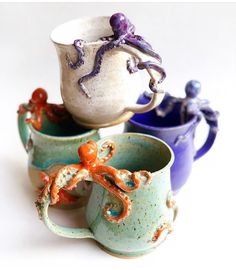 three ceramic cups with octopus figurines in them on a white surface, one is blue and the other has an orange octopus