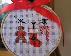 a cross stitch christmas ornament hanging from a hoop with a red ribbon on it