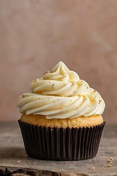 a cupcake with white frosting and sprinkles on top sitting on a wooden table