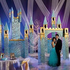 a man and woman standing in front of a blue castle with snow on the ground