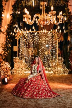 a woman in a red and gold bridal gown sitting on the floor with chandelier