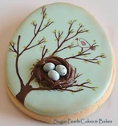 a decorated cookie with eggs in a nest on top of a tree branch and leaves