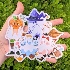 a hand holding several stickers in front of some green plants and bushes with pumpkins on them