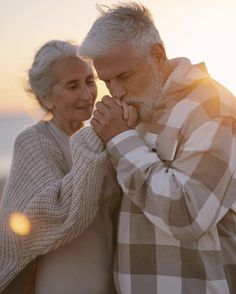 an older man and woman standing next to each other in front of the ocean at sunset