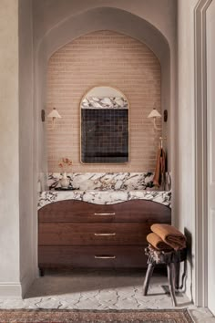 an arched doorway leads into a bathroom with marble counter tops and wooden stools on the floor