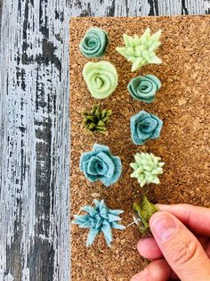 someone is holding up some felt flowers on a cork board with wood planks in the background