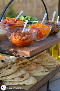 an assortment of food is displayed on a wooden platter with bowls and spoons