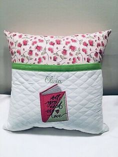 a white pillow with pink flowers and green trim on the side, sitting on a bed