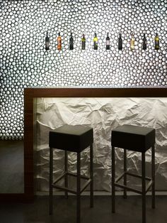 two bar stools sitting in front of a wall with bottles hanging from it's sides