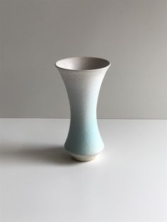 a white and blue vase sitting on top of a table next to a gray wall