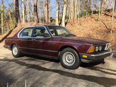 a maroon car parked on the side of a road in front of trees and bushes