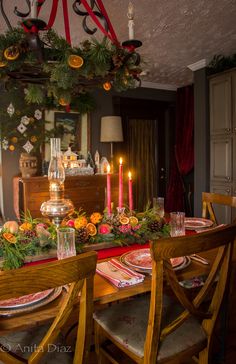 a dining room table set for christmas with candles and greenery on the table top