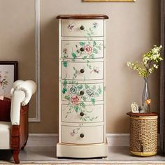 a white cabinet with flowers painted on it in a room next to a chair and table