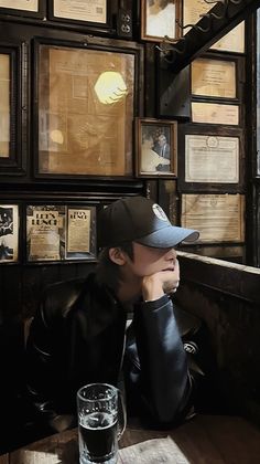 a man sitting at a table in front of a wall full of framed pictures and papers