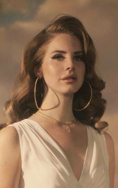 a woman wearing large hoop earrings and a white dress is looking at the camera with an intense look on her face