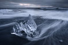 an iceberg floating in the ocean with waves crashing around it's base and breaking up