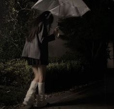 a woman holding an umbrella while walking down the street at night with her boots on