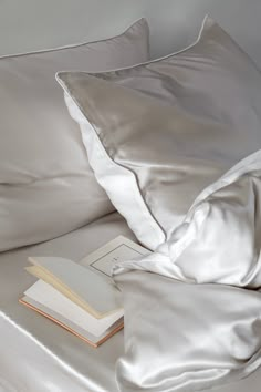 an open book on top of a bed with white sheets and pillow cases next to it