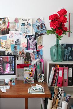 a desk with a computer monitor, keyboard and red flowers in a vase on it