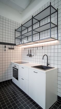 a kitchen with black and white tiles on the wall, sink and shelves above it