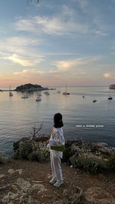 a woman standing on top of a rocky hillside next to the ocean with boats in the water