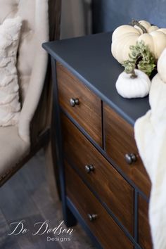 a black dresser with two white pumpkins on it and a chair in the background