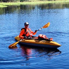 a man in an orange life jacket paddling a yellow kayak on the water