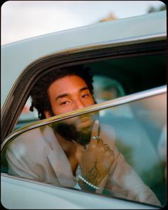 a man with dreadlocks sitting in a car and pointing to the side window