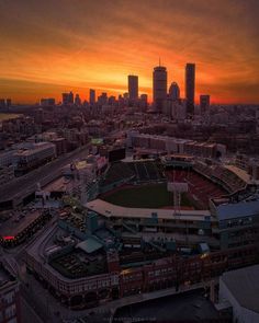 an aerial view of a baseball stadium with the sun setting in the background and city buildings