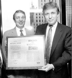 black and white photograph of two men holding up a framed poster in front of them