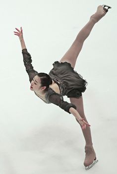 a female figure skating on the ice in a short skirt and tights, with her arms stretched out