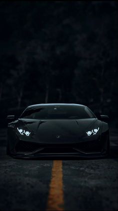 a black sports car parked on the side of a road in the dark with its lights on