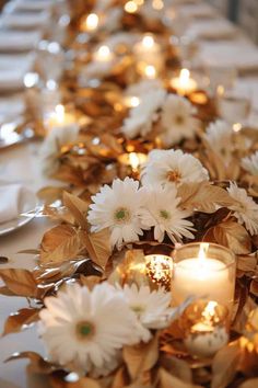 white flowers and candles on a table with gold foiled leaves around the centerpiece