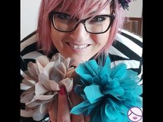 a woman with pink hair and black glasses holding two flower brooches in front of her face