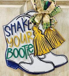 a door hanger that says shake your bootie on it and has a shoe with a tassel hanging from the front