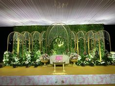 a stage set up for a wedding with flowers and greenery on the wall behind it