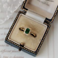 an engagement ring with a green stone sits in a box on top of a piece of paper