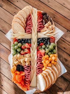 a platter filled with cheese, crackers, fruit and meats on top of a wooden table