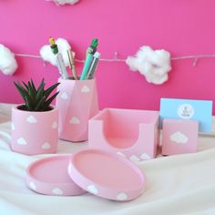 pink and white desk accessories with clouds on the wall behind them, including pen holders