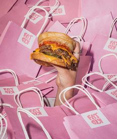 a person holding up a hamburger in front of pink bags