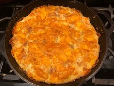 a cheese pizza sitting on top of a stove next to a frying pan filled with food