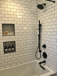 a white tiled bathroom with black fixtures and shower faucet, hand held shower head