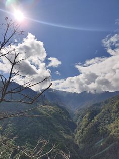 the sun shines brightly over mountains and trees in the foreground, while clouds loom overhead