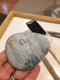 a person holding a rock with a toothpick in it's hand and some other items on the table