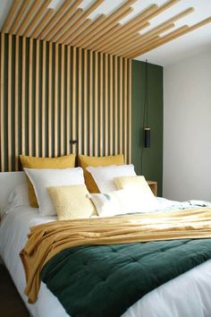 a bed with white and green sheets in a bedroom next to a wall mounted wooden slatted headboard