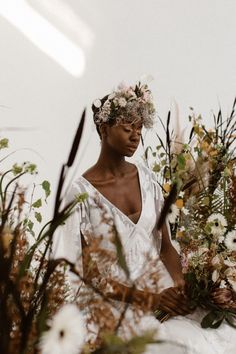 a woman in white dress sitting on the ground surrounded by plants and flowers with her eyes closed