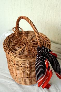 a wicker basket sitting on top of a bed next to a red and white striped scarf