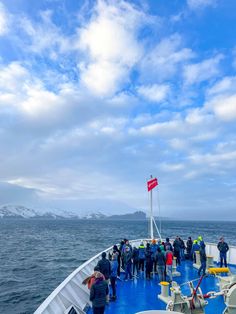 people are standing on the deck of a boat in the ocean, with mountains in the background