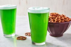 two glasses filled with green liquid and pretzels next to each other on a table